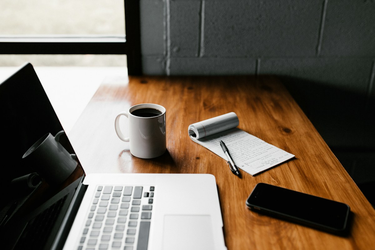 Laptop, ponsel, dan buku catatan di atas meja kayu